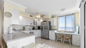 Cocina moderna con armarios blancos, un refrigerador de acero inoxidable y una zona de comedor con una silla y mesa blancos.