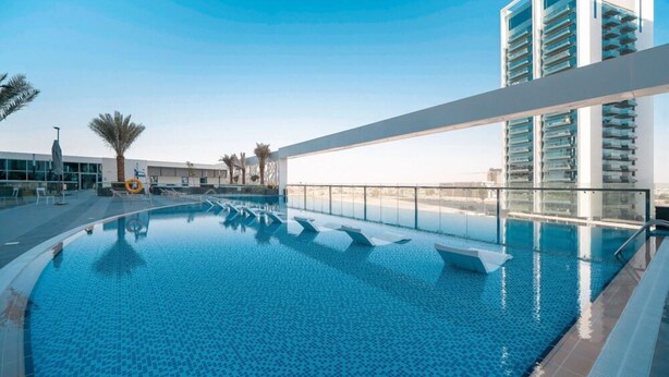 A modern hotel with a rooftop infinity pool, a glass balustrade, and a high-rise building in the background.