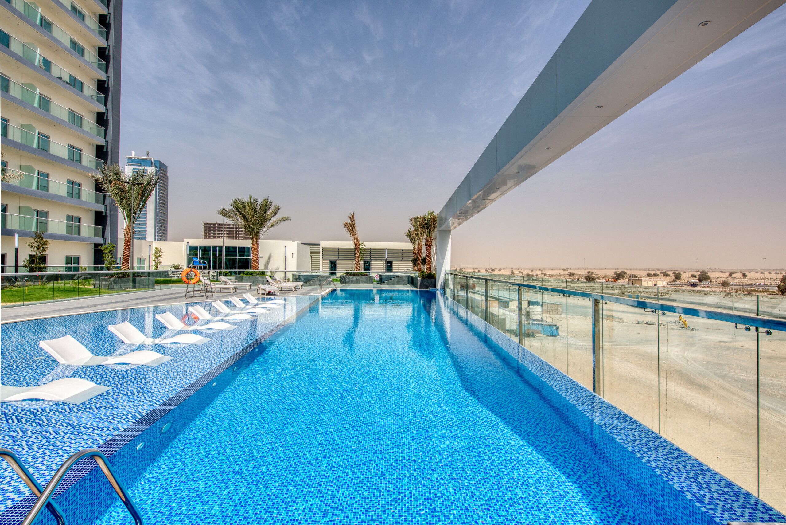 A rooftop pool with clear blue water, surrounded by modern buildings and palm trees.