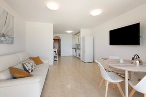 Un salon moderne avec un canapé blanc, un téléviseur à écran plat fixé au mur et un coin repas comprenant une table et des chaises.