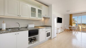 A modern kitchen with white cabinets, a granite countertop, a built-in oven, and a dining area with a table and chairs.