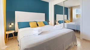 A bedroom with a large bed, a bedside table, a mirror, and a window with curtains.