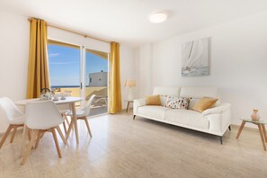 Un salon moderne avec un canapé blanc, une table à manger avec des chaises, une lampe et un tableau au mur.