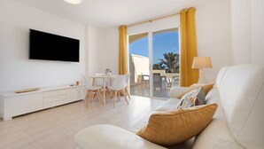 A modern living room with a flat-screen TV, a sofa, a dining area with chairs, and a view through a glass door.