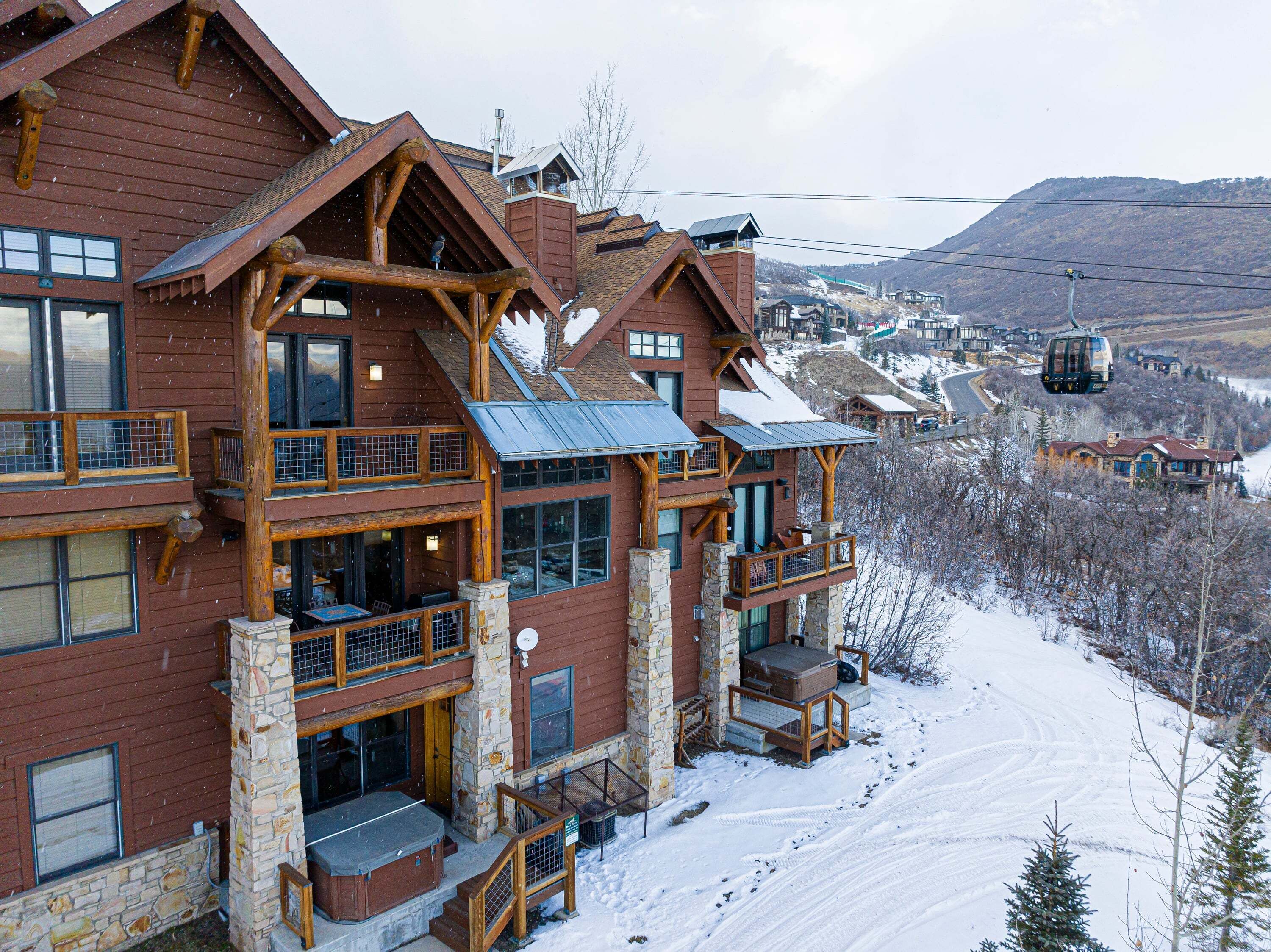 A multi-story lodge with stone pillars, balconies, and a ski lift in the background.