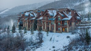 Ein großes, mehrstöckiges Chalet mit symmetrischem Dach und mehreren Balkonen, umgeben von schneebedeckten Bäumen und einer Bergkulisse.
