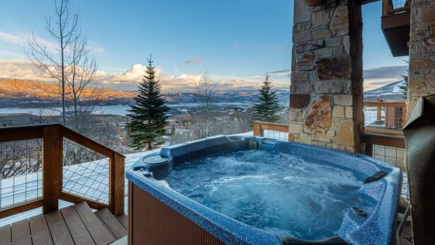 Ein Whirlpool auf einer Holzterrasse mit einer Steinsäule mit Blick auf eine verschneite Landschaft und ein Gewässer.