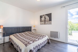 Un dormitorio con una cama, una mesita de noche, una lámpara, un radiador y una ventana con vistas.