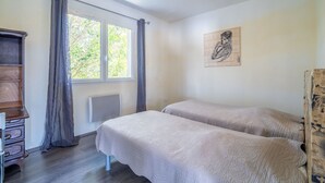 A room with two beds, a window with curtains, a radiator, a wooden dresser, and a wall painting. - Villa 'Piscine Privée Proche Plages' with Private Pool, Private Terrace and Wi-Fi (Montséret)
