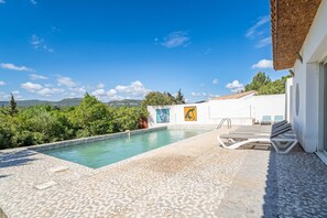 Una piscina con solárium empedrado, sillas de descanso y obras de arte en la pared.