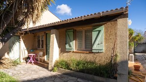 Une maison avec une terrasse carrelée, des volets verts et une petite table avec des chaises.