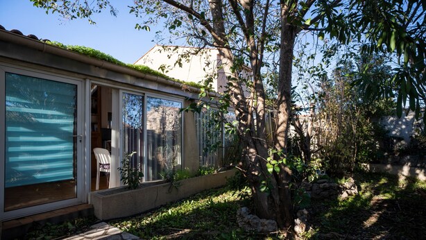 Une maison avec une porte-fenêtre coulissante, un chemin de pierres et un arbre dans le jardin.