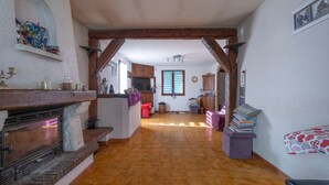 Un vaste espace de vie doté d’une cheminée, de poutres apparentes, d’une cuisine et d’un escalier menant à un niveau supérieur.