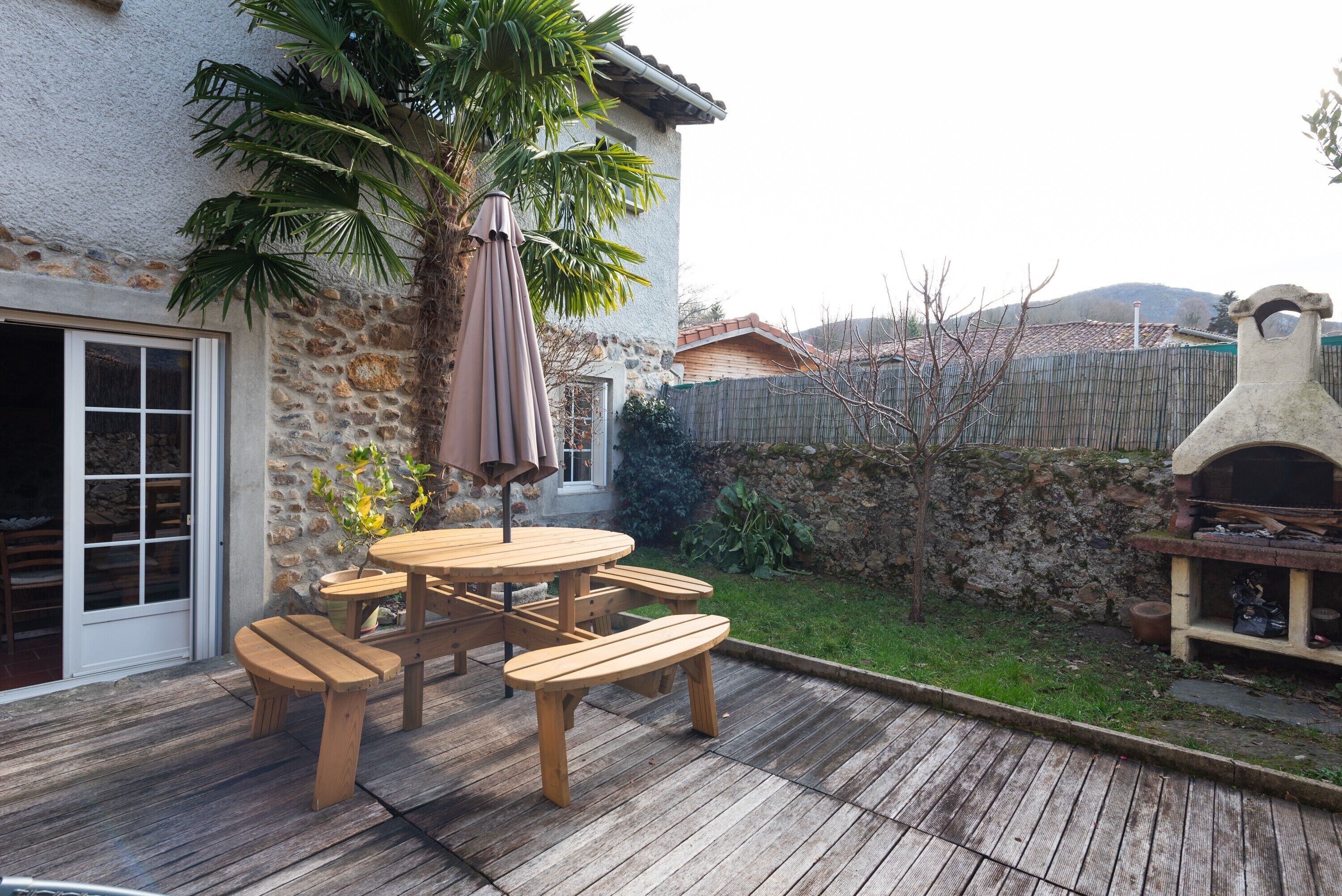Un patio con mobiliario de madera, una palmera y un muro de piedra.