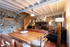 A rustic interior with a wooden dining table, a staircase, stone walls, and a leather sofa.
