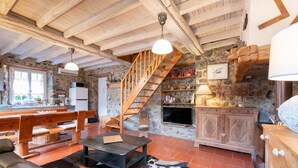 A rustic interior with a wooden staircase, stone walls, a fireplace, and a dining area.