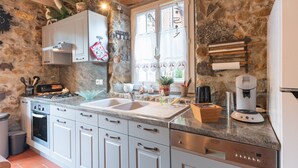A kitchen with granite countertops, white cabinets, a built-in oven, a coffee maker, and a stone wall.