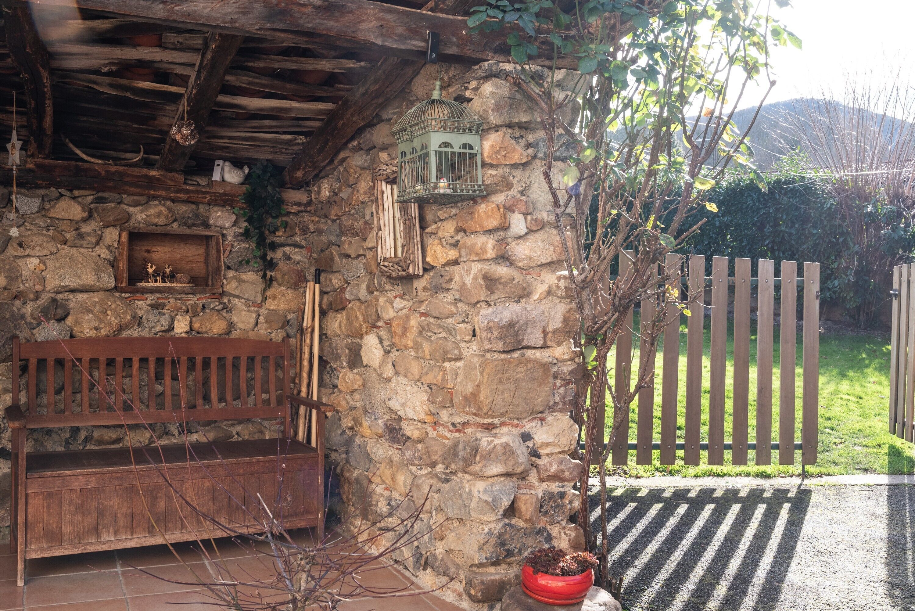 A rustic stone wall, wooden bench, birdcage, and a wooden fence.
