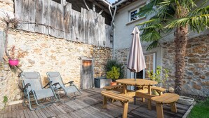 A wooden deck with outdoor furniture, a stone wall, and a palm tree.
