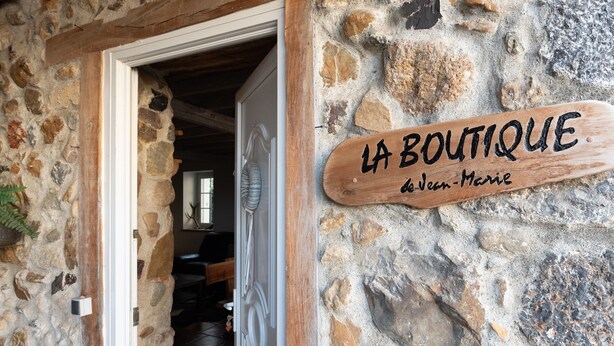 A stone building with a wooden sign reading 'LA BOUTIQUE de Jean-Marie' and a doorway leading inside.