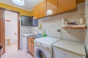 A compact kitchen with a washing machine, a sink, wooden cabinets, and a tiled backsplash.