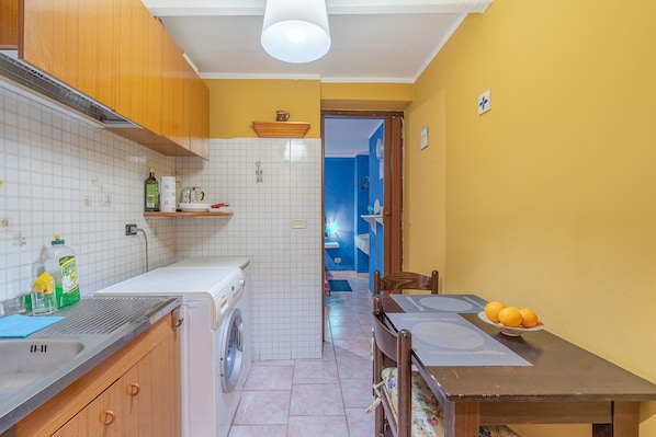 A kitchen with a washing machine, a sink, and a dining area with a table and chairs.