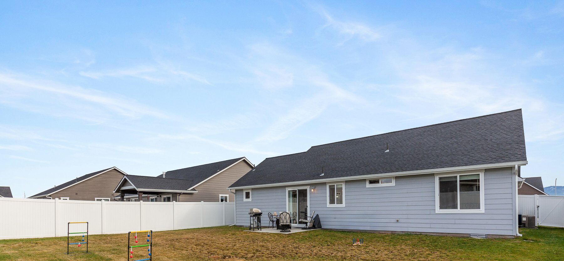 A residential house with a grey exterior, a dark roof, and a fenced backyard.