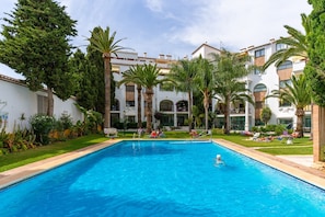 A swimming pool surrounded by palm trees and a multi-story building with balconies. - Apartment 'Puebla Lucia Fuengirola' with Shared Pool, Wi-Fi and Air Conditioning (Fuengirola)
