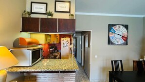 Cocina compacta con microondas, estufa y refrigerador. Cuenta con una zona de comedor con mesa y sillas.