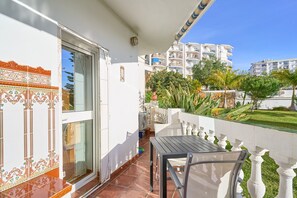 A balcony with a table and chairs, a sliding glass door, and a view of a residential area with buildings and greenery.
