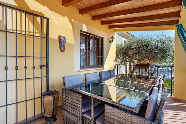 A patio with a glass-top table and wicker chairs, a metal gate, and a window with a view of the outdoors.