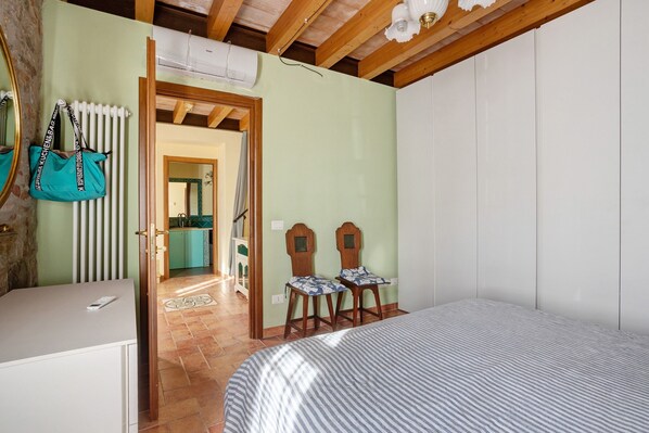 A bedroom with a bed, a desk, a chair, a radiator, and a door leading to a bathroom.