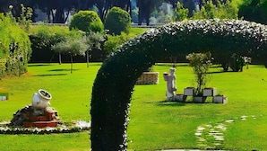 Un jardín cuidado con setos curvados, una estatua y un pequeño árbol en una jardinera.