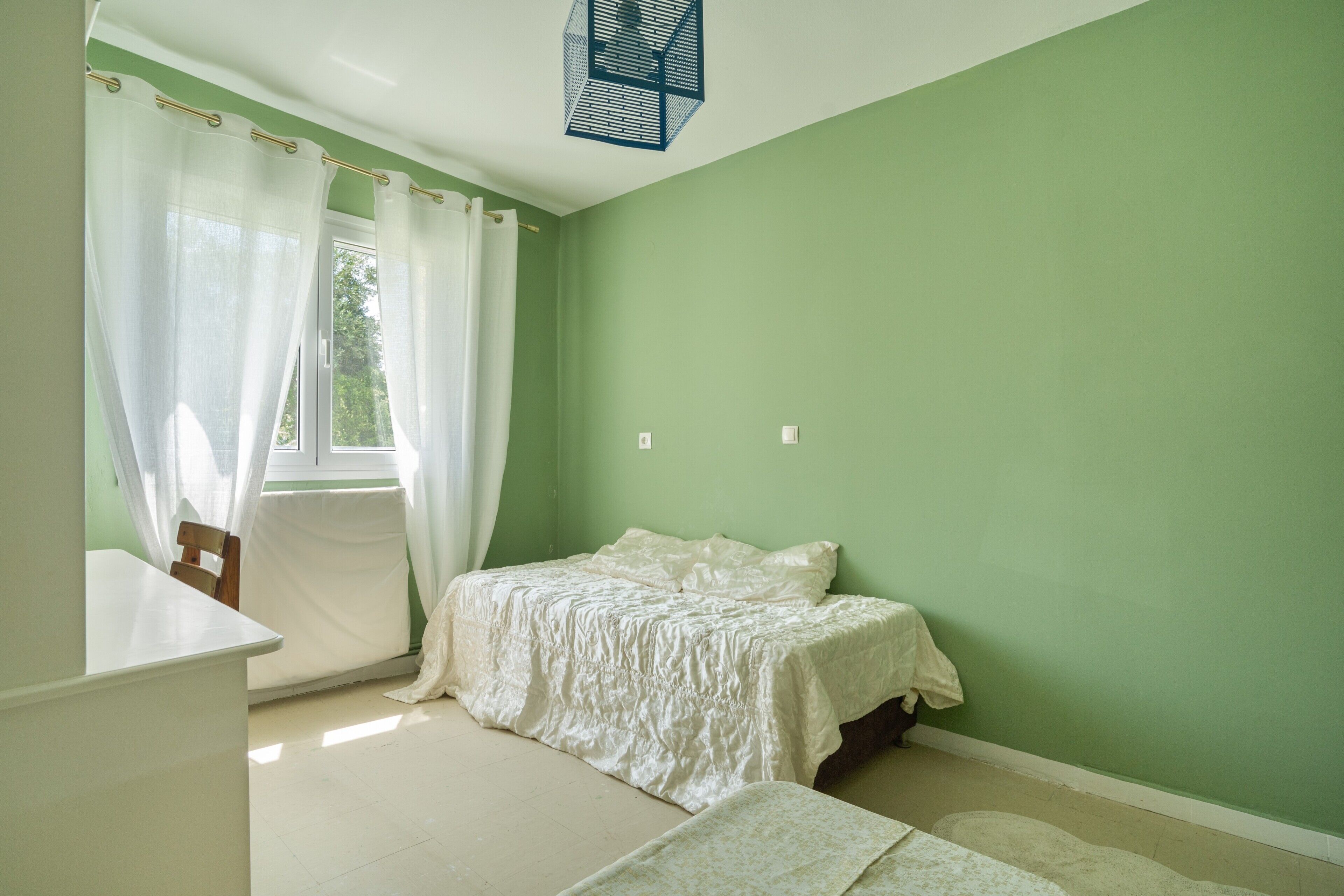 A bedroom with a bed, a chair, a desk, and a window with curtains.