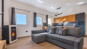 A modern living room with a grey sectional sofa, a wood-burning stove, and a kitchen area with wooden cabinets and a microwave. - Apartment '42A' with Mountain Views, Private Terrace and Wi-Fi (Sierra Nevada)