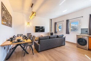 A modern living room with a dining area, a gray sofa, a flat-screen TV, and a washing machine. - Apartment '42A' with Mountain Views, Private Terrace and Wi-Fi (Sierra Nevada)