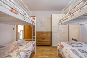 Huoneessa on kerrossängyt, puinen lipasto ja ovi, joka johtaa portaikkoon.