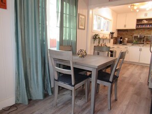 Uma área de refeições com mesa e cadeiras, uma cozinha ao fundo e uma janela com cortinas.