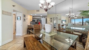 A spacious dining area with a glass-top table, wooden benches, and a chandelier. - WHITE CAPS 105 - AFFORDABLE BEACHFRONT RELAXATION! (Orange Beach)