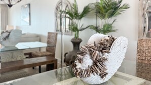 A modern living room with a glass coffee table, a sofa, and a decorative shell sculpture. - WHITE CAPS 105 - AFFORDABLE BEACHFRONT RELAXATION! (Orange Beach)