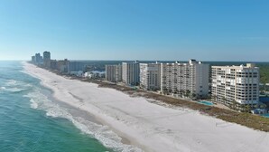 A beachfront hotel with multiple high-rise buildings, a sandy beach, and a clear blue sky. - WHITE CAPS 105 - AFFORDABLE BEACHFRONT RELAXATION! (Orange Beach)