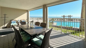 A balcony with a dining table, chairs, and a view of a pool and ocean. - WHITE CAPS 105 - AFFORDABLE BEACHFRONT RELAXATION! (Orange Beach)