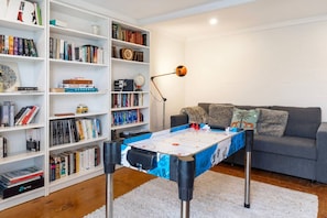 Une pièce avec une table de baby-foot, un canapé gris et une bibliothèque remplie de livres.