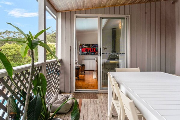 Un balcon doté d’une terrasse en bois, d’une table blanche et d’un canapé.