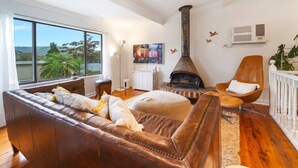 Una sala de estar acogedora con un sofá de cuero, piso de madera, chimenea, ventana grande y vistas al exterior.