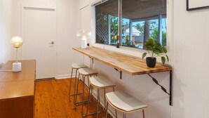 Una cocina con encimera de madera, taburetes de bar, una planta en maceta y una ventana con vistas a casas.