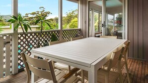 Un espacio exterior techado con una mesa y sillas, una terraza de madera y vistas a zonas verdes y árboles.
