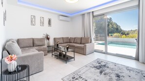 Un salon moderne avec un canapé, une table basse et une grande fenêtre donnant sur la piscine.