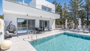 Un bâtiment moderne à deux étages doté d’une piscine, d’un espace extérieur aménagé et d’un balcon orné d’une statue.