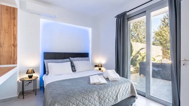 Une chambre moderne avec un grand lit, une table de chevet avec une lampe et une porte-fenêtre coulissante donnant sur l’extérieur.